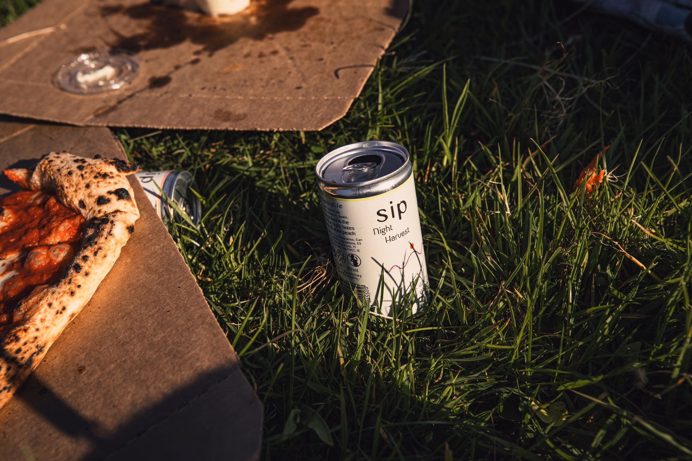 SIP Night Harvest can next to a slice of pizza on grass